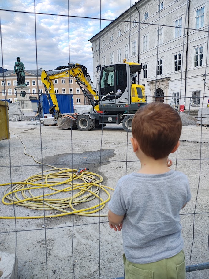 Un bambino osserva da vicino un escavatore gommato giallo in una piazza