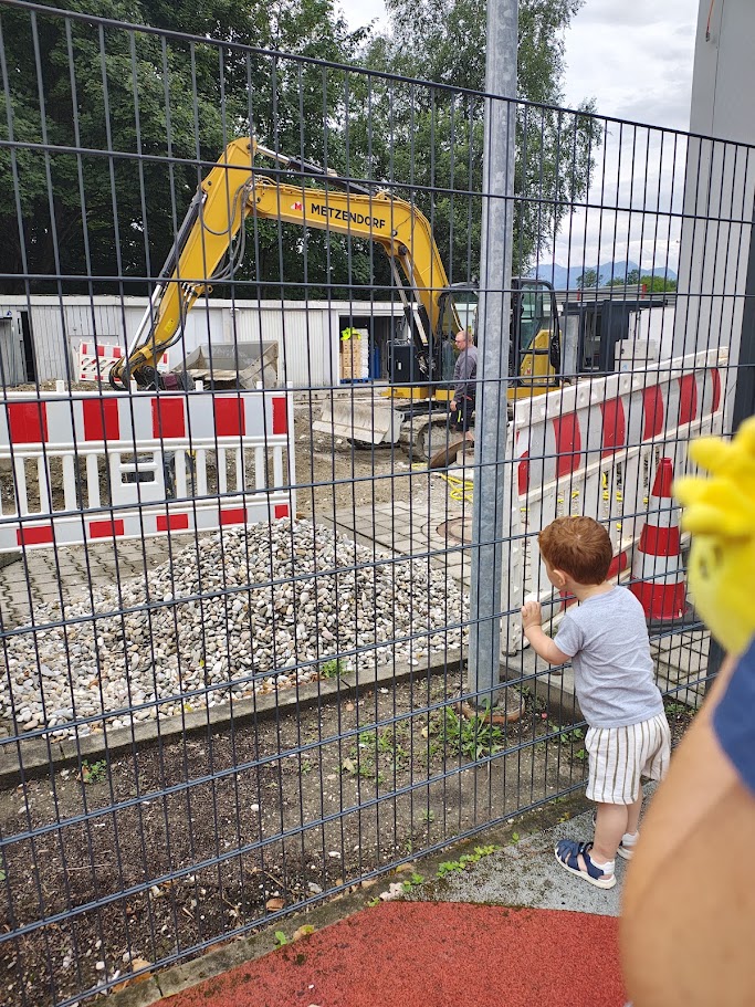 Un bambino in piedi alla recinzione osserva un escavatore al lavoro