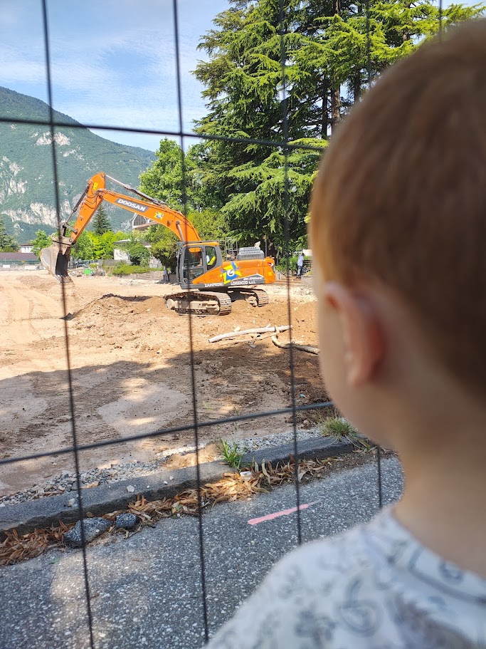 Un bambino osserva un escavatore arancione in manovra su un terreno di montagna